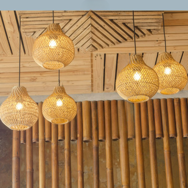 Cinq luminaires suspendus en rotin croisé en forme de boule resserrés par un cône au niveau de l'ampoule. Installé sur un plafond en planches de bois qui créer une décoration. on voit aussi des bambous peint couleur bois qui forme un sorte de mur.