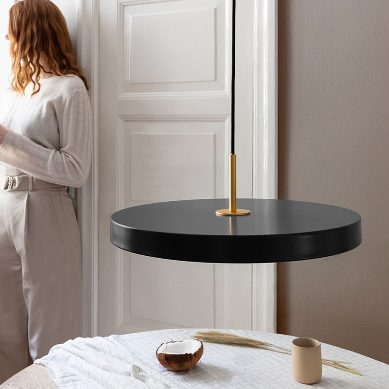 Luminaire cuisine suspendu LED en métal en forme de disque installé au dessus d'une table de cuisine dans laquelle se trouve une jeune femme