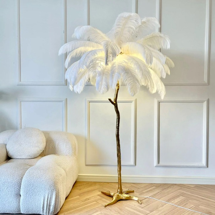 Luminaire sur pied style palmier grandes plumes blanc présenté à côté d'un canapé de la même couleur